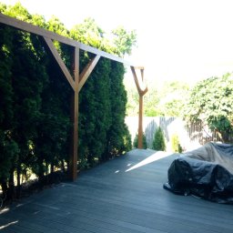 Sebastian Cymba - Nowoczesny taras z kompozytowych desek w odcieniach szarości, z drewnianą pergolą i żywopłotem z tui, częściowo zakryty plandeką.