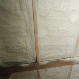 Poddasze ocieplone białą pianką poliuretanową, widoczne drewniane elementy konstrukcyjne dachu.