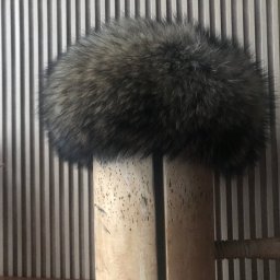 Usługi krawiecko-kuśnierskie - Puszysta, okrągła czapka z futra w odcieniach brązu i szarości, ustawiona na drewnianej formie, na tle ściany z pionowymi paskami.