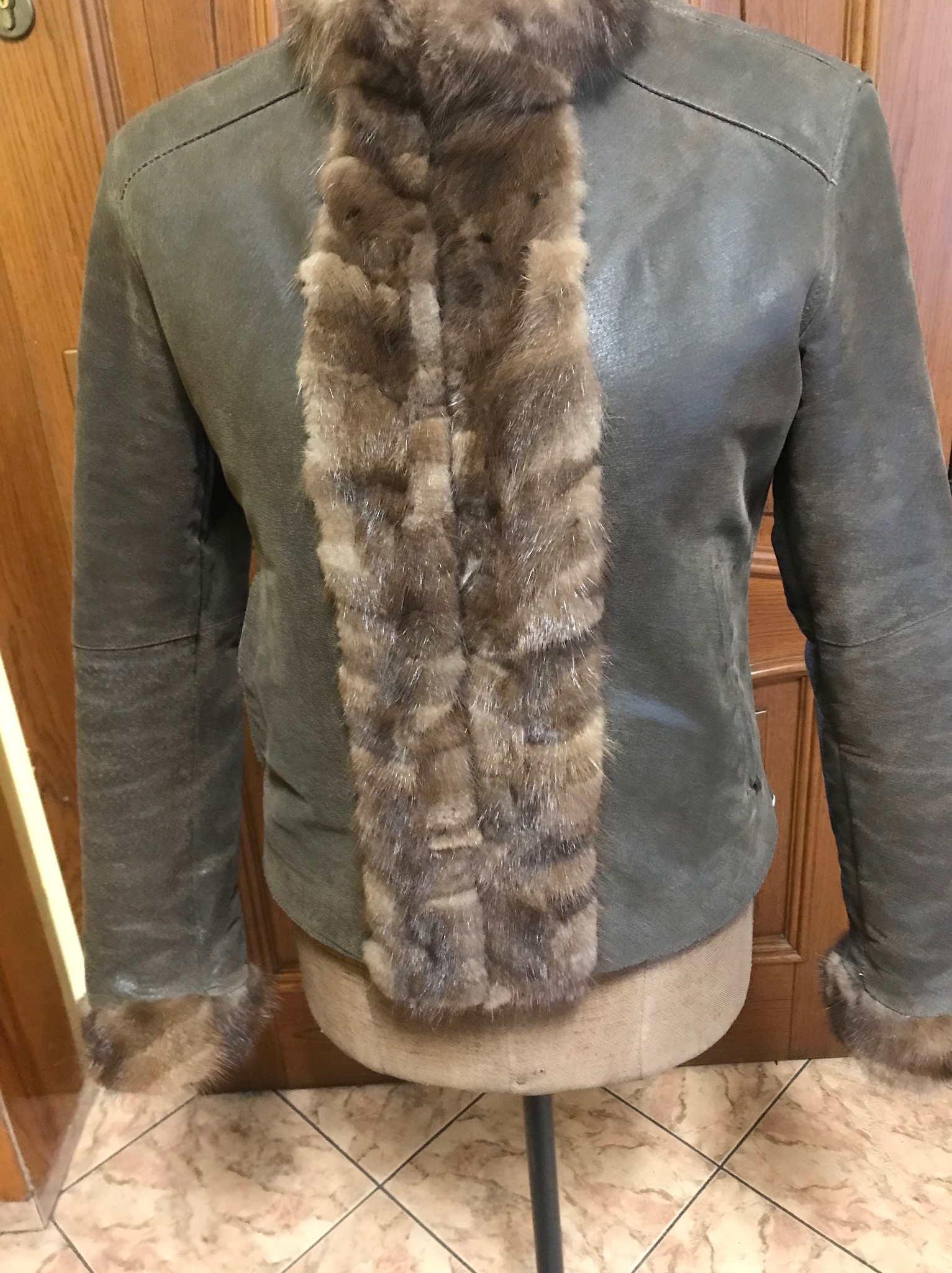 Szaro-zielona kurtka z zamszu z brązowym futrzanym kołnierzem i mankietami, prezentowana na manekinie.