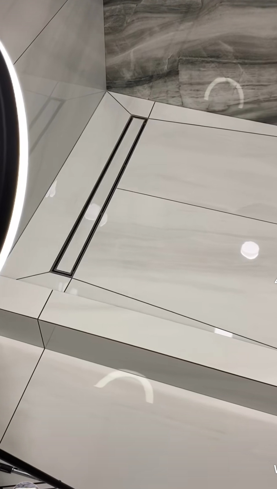 Nowoczesna łazienka z białymi płytkami, liniowym odpływem podłogowym i marmurową ścianą w odcieniach szarości.