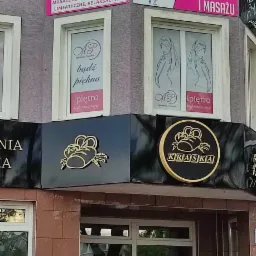 Zewnętrzny widok budynku z szyldami salonu kosmetycznego i masażu 'Studio Kosmetyczne i Masażu' oraz 'Studio Masażu', z ofertą zabiegów na twarz i ciało, masaży leczniczych i sportowych, oraz logo...