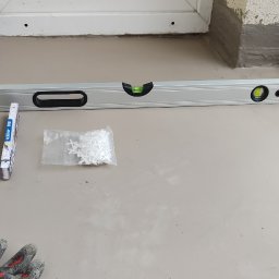 Tomasz Czaja - Balkon w trakcie prac wykończeniowych: poziomica, krzyżyki dystansowe, płytka i dłoń glazurnika przy balustradzie