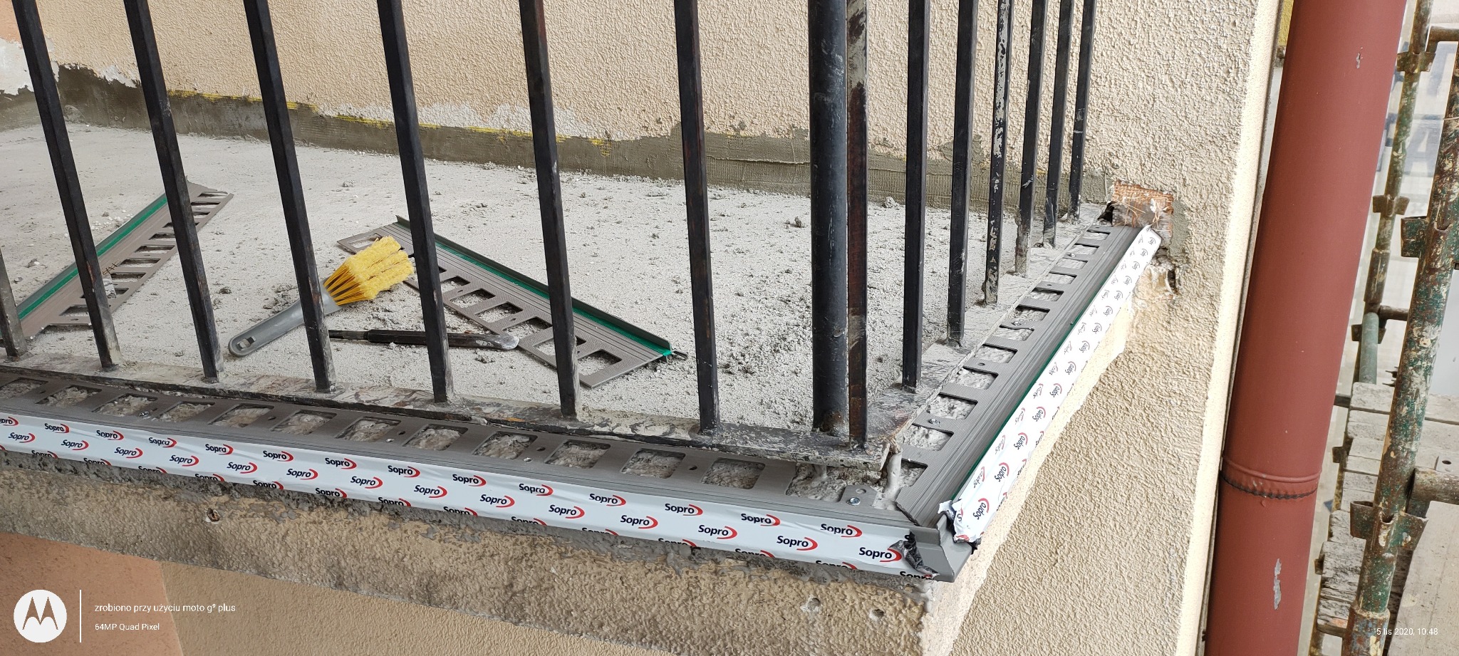 Montaż profilu okapowego na balkonie z widocznymi narzędziami i szczotką do czyszczenia, etap prac wykończeniowych.