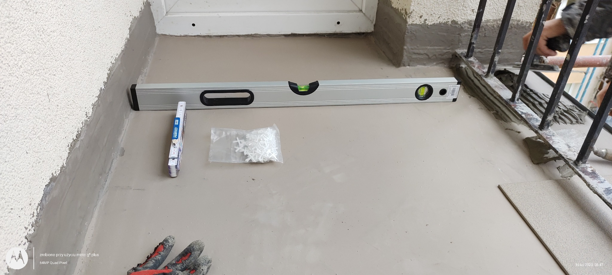 Balkon w trakcie prac wykończeniowych: poziomica, krzyżyki dystansowe, płytka i dłoń glazurnika przy balustradzie
