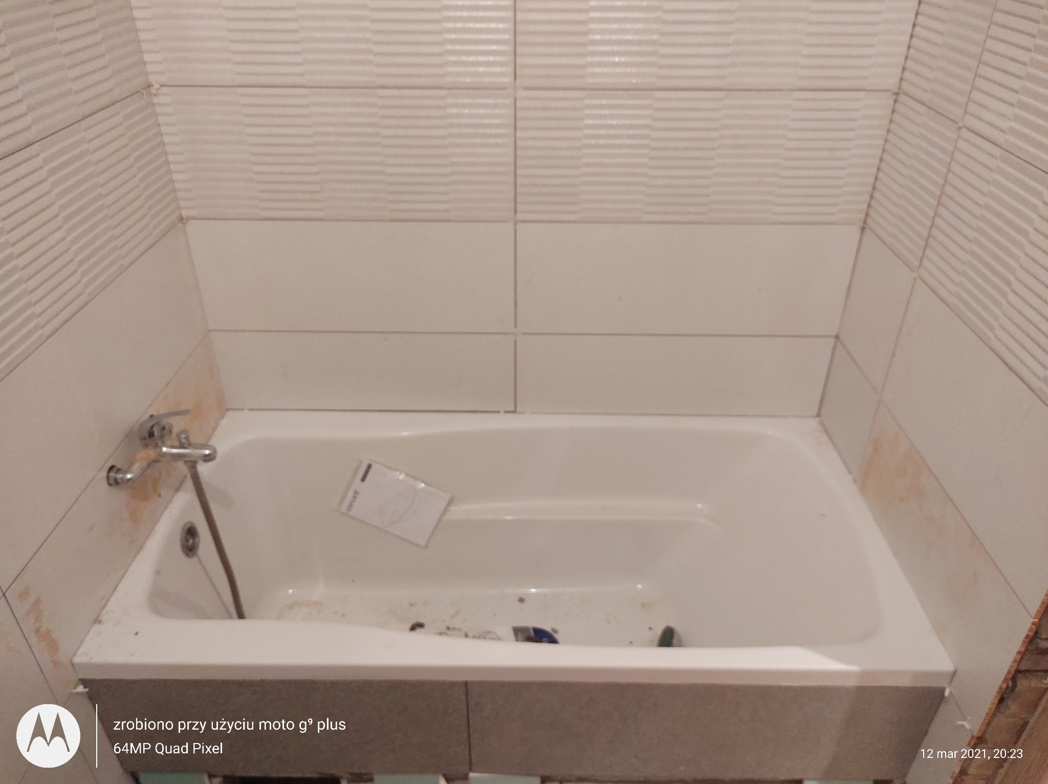 Biała wanna w trakcie obkładania płytkami, widoczne ślady zaprawy na ścianie i w wannie, oraz akcesoria glazurnicze wewnątrz wanny.