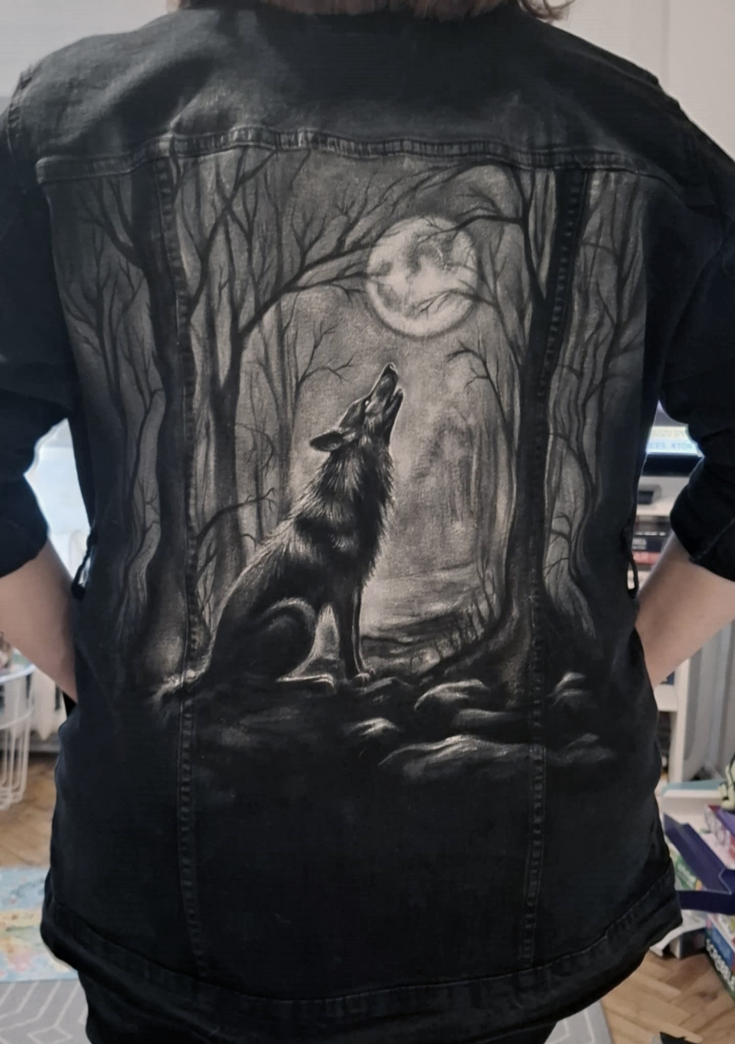 Czarna kurtka jeansowa z ręcznie malowanym wilkiem wyjącym do księżyca w leśnej scenerii, unikatowy wzór na plecach, widok z tyłu.