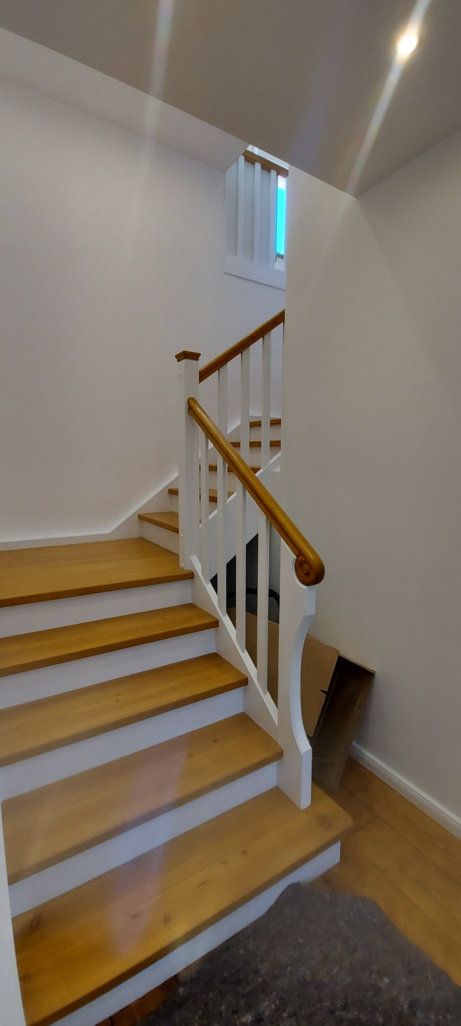 Jasne, drewniane schody z białymi podstopnicami i poręczą z naturalnego drewna w minimalistycznym wnętrzu.