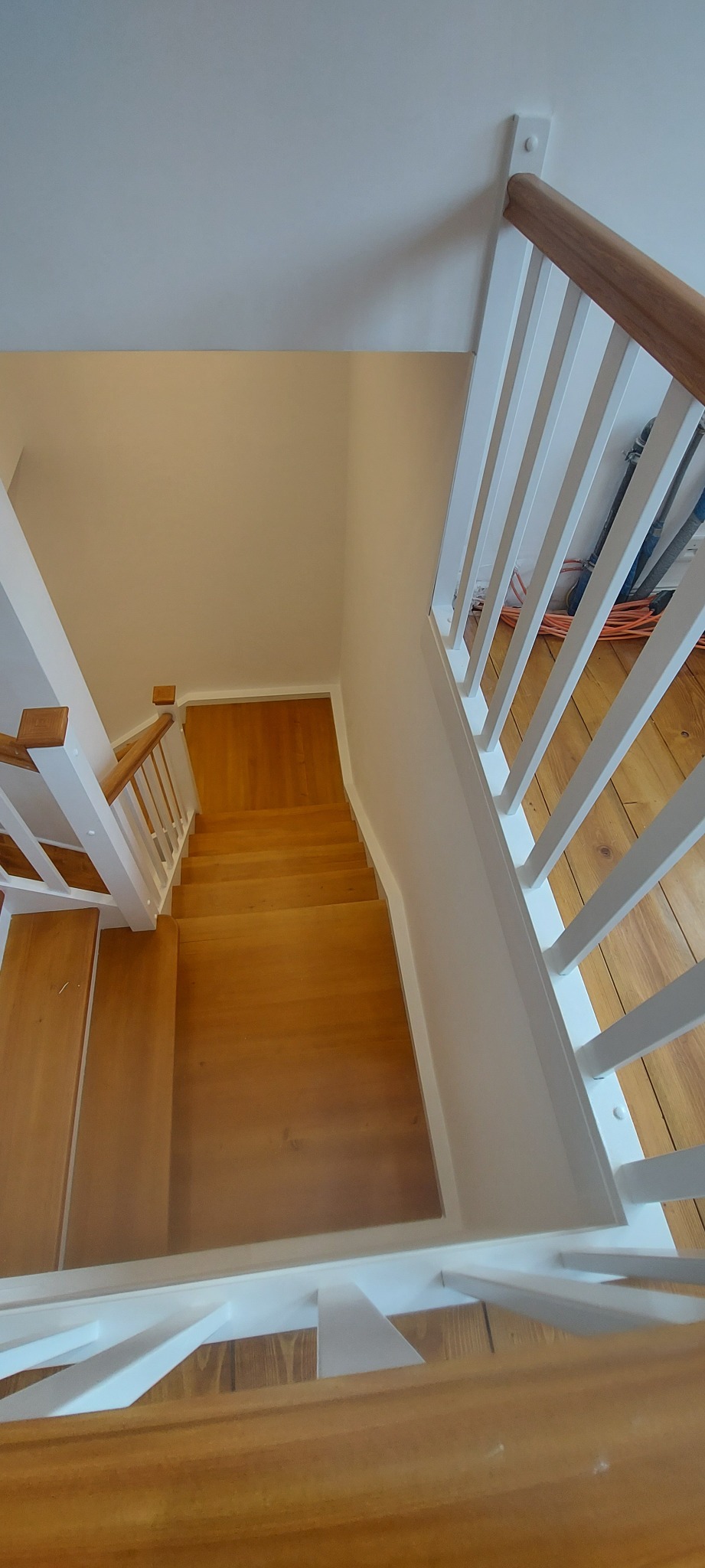 Widok z góry na drewniane schody z białymi balustradami i drewnianymi poręczami, po cyklinowaniu i malowaniu.