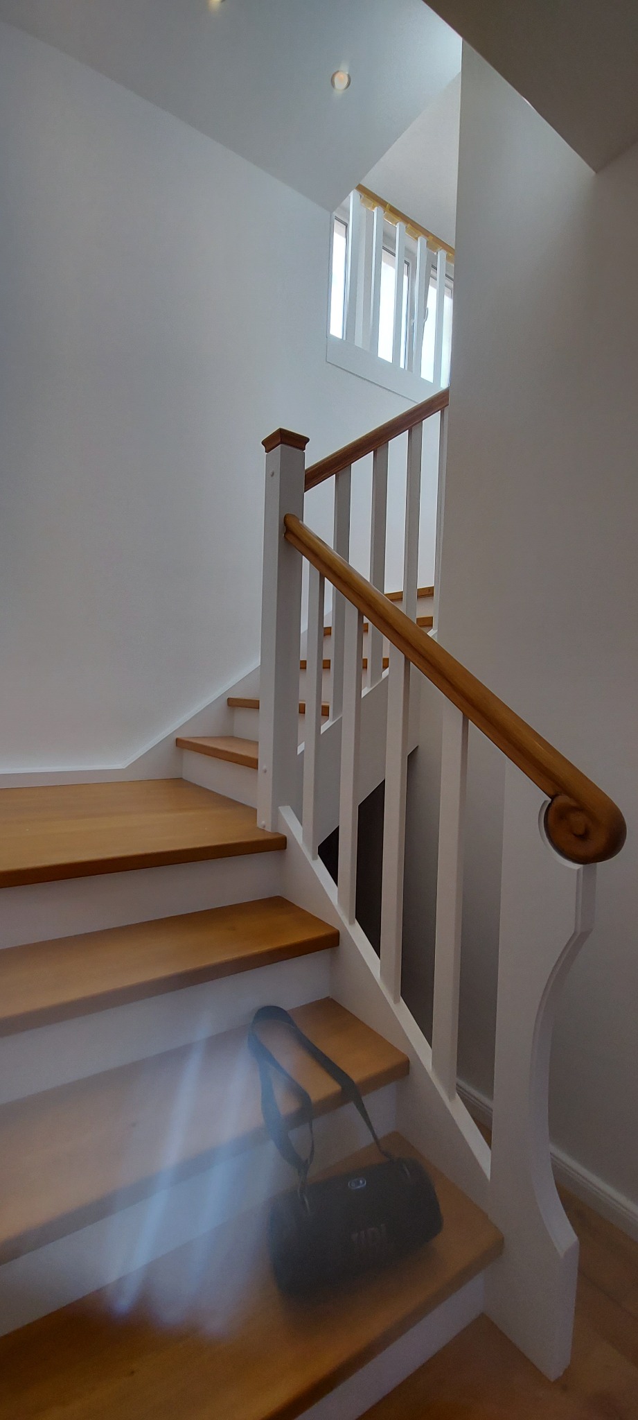 Jasne drewniane schody z białymi podstopnicami i balustradą, torba sportowa leży na jednym ze stopni.