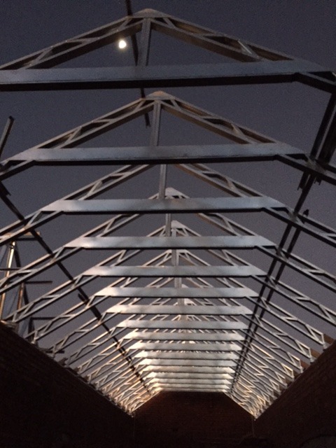 Konstrukcja dachu z drewnianych belek widziana od wewnątrz, w tle nocne niebo z widocznym księżycem.