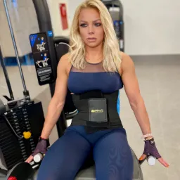 Kobieta w pasie treningowym wykonuje ćwiczenie na maszynie do wyprostu nóg w Bydgoszczy. Trening siłowy z trenerem personalnym, widoczne obciążenia.