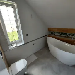 Nowoczesna łazienka na poddaszu ze skośnym oknem, wolnostojącą białą wanną i minimalistyczną armaturą.