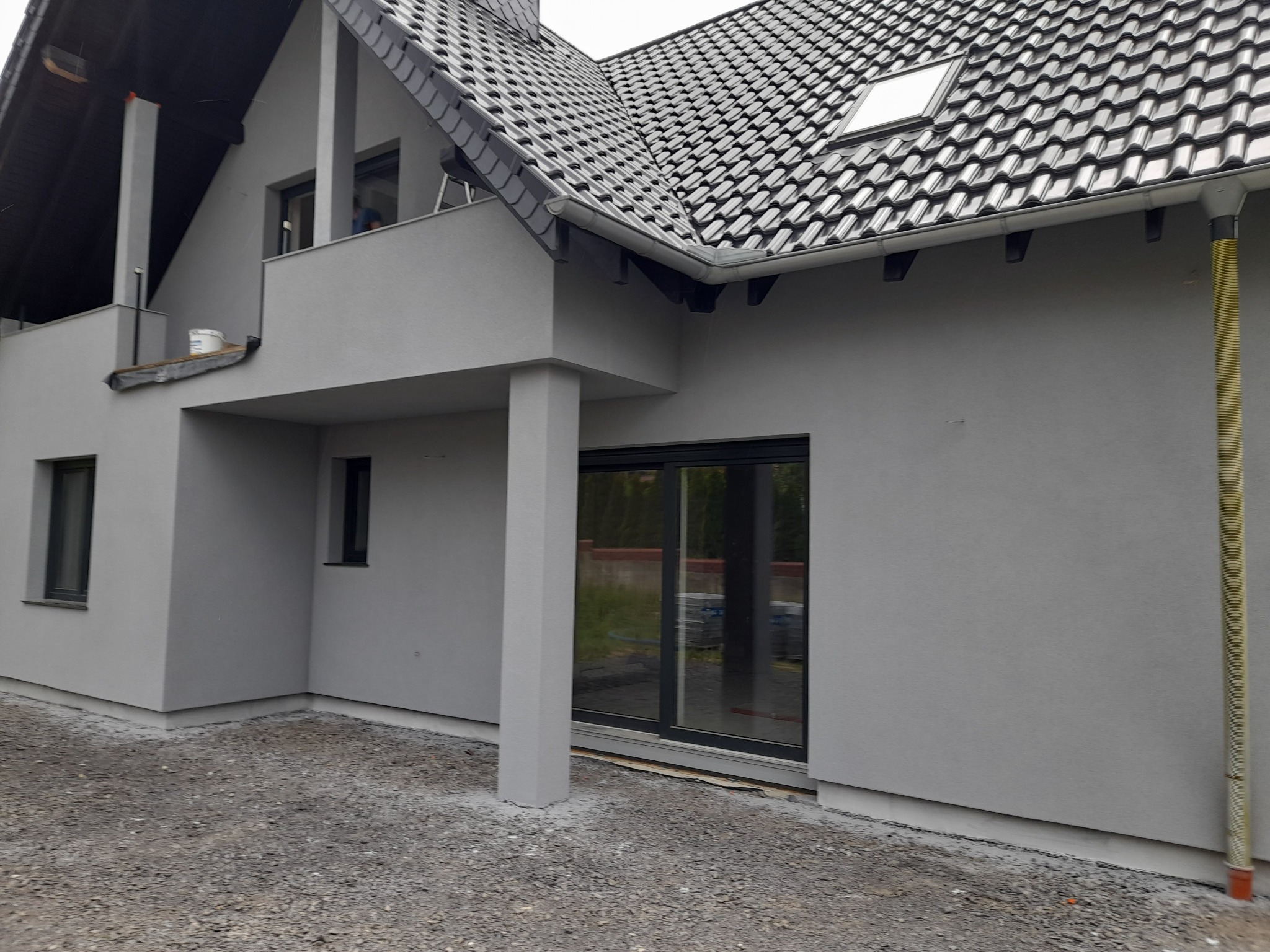 Szary dom jednorodzinny po świeżym tynkowaniu elewacji, z widoczną elewacją, oknami, dachem z dachówki i gruntem wokół budynku.