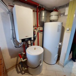 N-Energia - Kompaktowa kotłownia z wiszącym piecem Viessmann, dwoma zbiornikami akumulacyjnymi i bojlerem, instalacja z rur miedzianych i PCV, widoczne manometry i zawory.