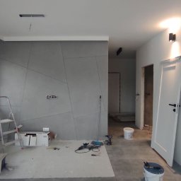 Firma Usługowo-Transportowa Egor Ermolenko - Wnętrze w trakcie prac wykończeniowych: ściana z dekoracyjną strukturą, widoczne narzędzia, drabina, nieotynkowane otwory drzwiowe, surowy beton na podłodze.