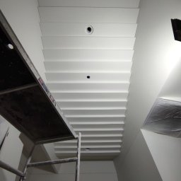 Firma Usługowo-Transportowa Egor Ermolenko - Biały, kasetonowy sufit z oświetleniem punktowym w trakcie prac, widoczny fragment rusztowania i zabezpieczona folią ściana.