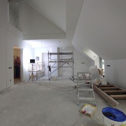 Firma Usługowo-Transportowa Egor Ermolenko - Poddasze w trakcie prac przygotowawczych do dalszego etapu wykończenia, widoczne rusztowania, drabiny, wiadra i narzędzia malarskie, ściany i skosy przygotowane pod dalsze prace wykończeniowe.
