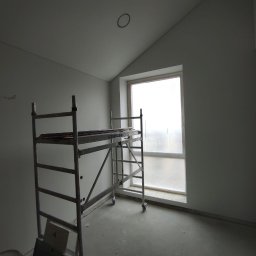 Firma Usługowo-Transportowa Egor Ermolenko - Wnętrze pokoju ze ścianami przygotowanymi do dalszych prac wykończeniowych, widoczne rusztowanie i okno zabezpieczone folią.