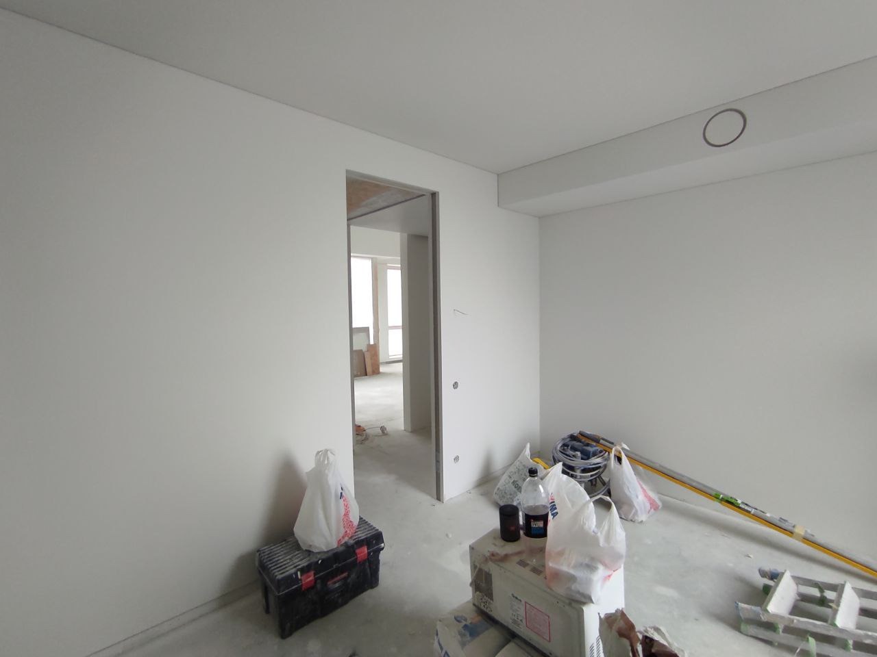 Wnętrze w trakcie remontu: świeżo pomalowane białe ściany, widoczne narzędzia i materiały budowlane, otwarte przejście do kolejnego pomieszczenia.
