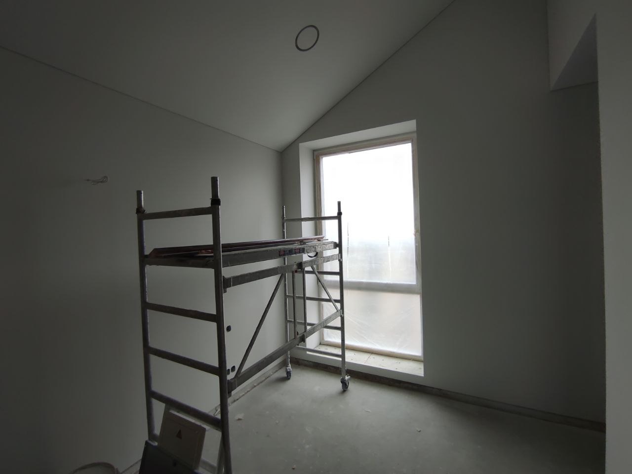 Wnętrze pokoju ze ścianami przygotowanymi do dalszych prac wykończeniowych, widoczne rusztowanie i okno zabezpieczone folią.