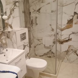 AUTOFIX - Wykończona łazienka z kabiną typu walk-in, marmurowymi płytkami na ścianach, białą armaturą i chromowaną deszczownicą. Nowoczesne i eleganckie wnętrze.