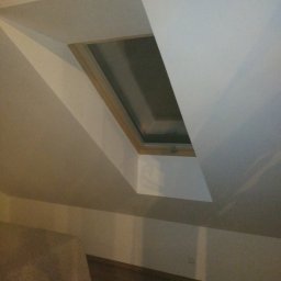 AUTOFIX - Poddasze z oknem dachowym w drewnianej ramie, świeżo po malowaniu na biało. Widoczny fragment podłogi i łóżka. Ujęcie z dołu.