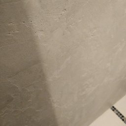 AUTOFIX - Szara ściana z efektem dekoracyjnym w łazience, widoczny fragment mozaiki. Bliski kadr, oświetlenie punktowe podkreśla fakturę ściany.