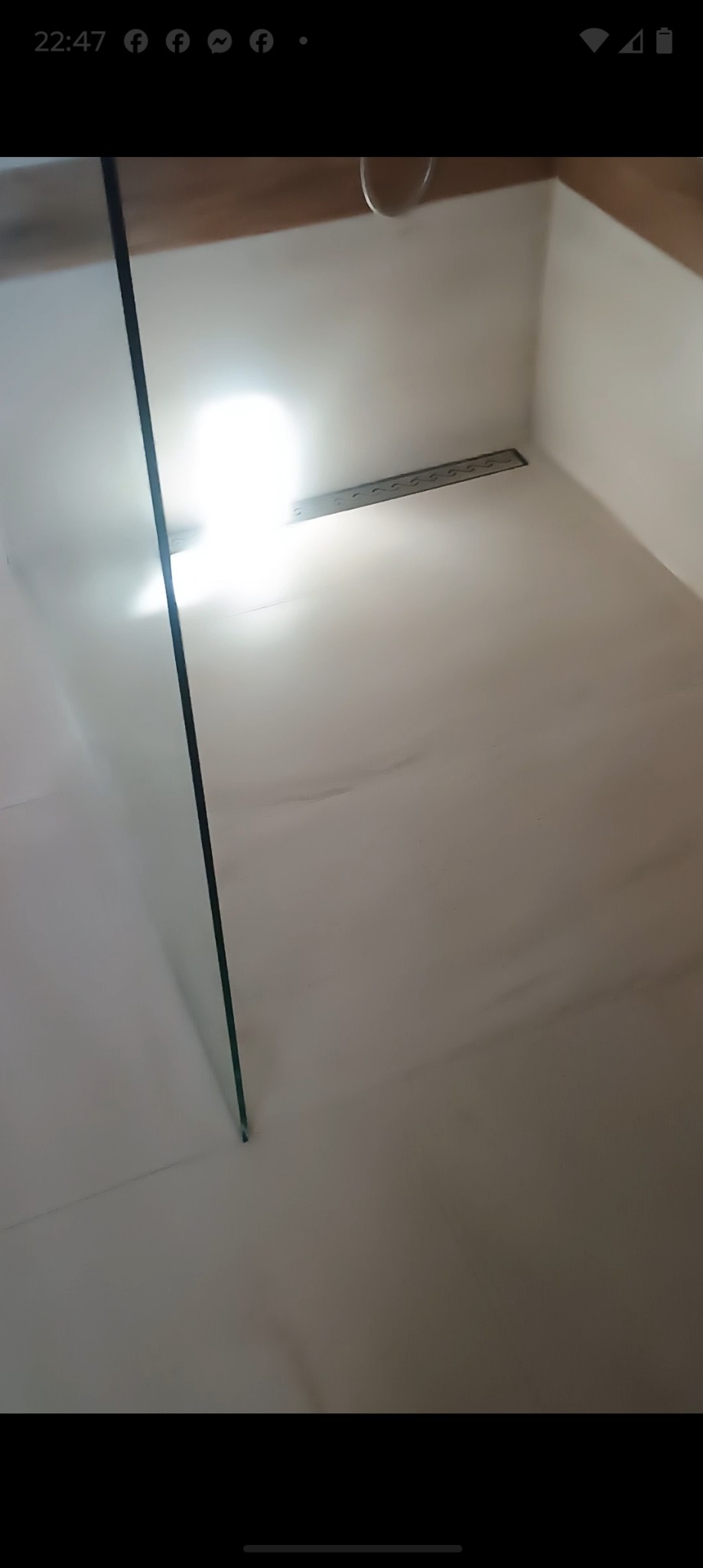 Biały brodzik z odpływem liniowym i szklaną ścianką kabiny, widok z góry. Minimalistyczny design, jasne oświetlenie.