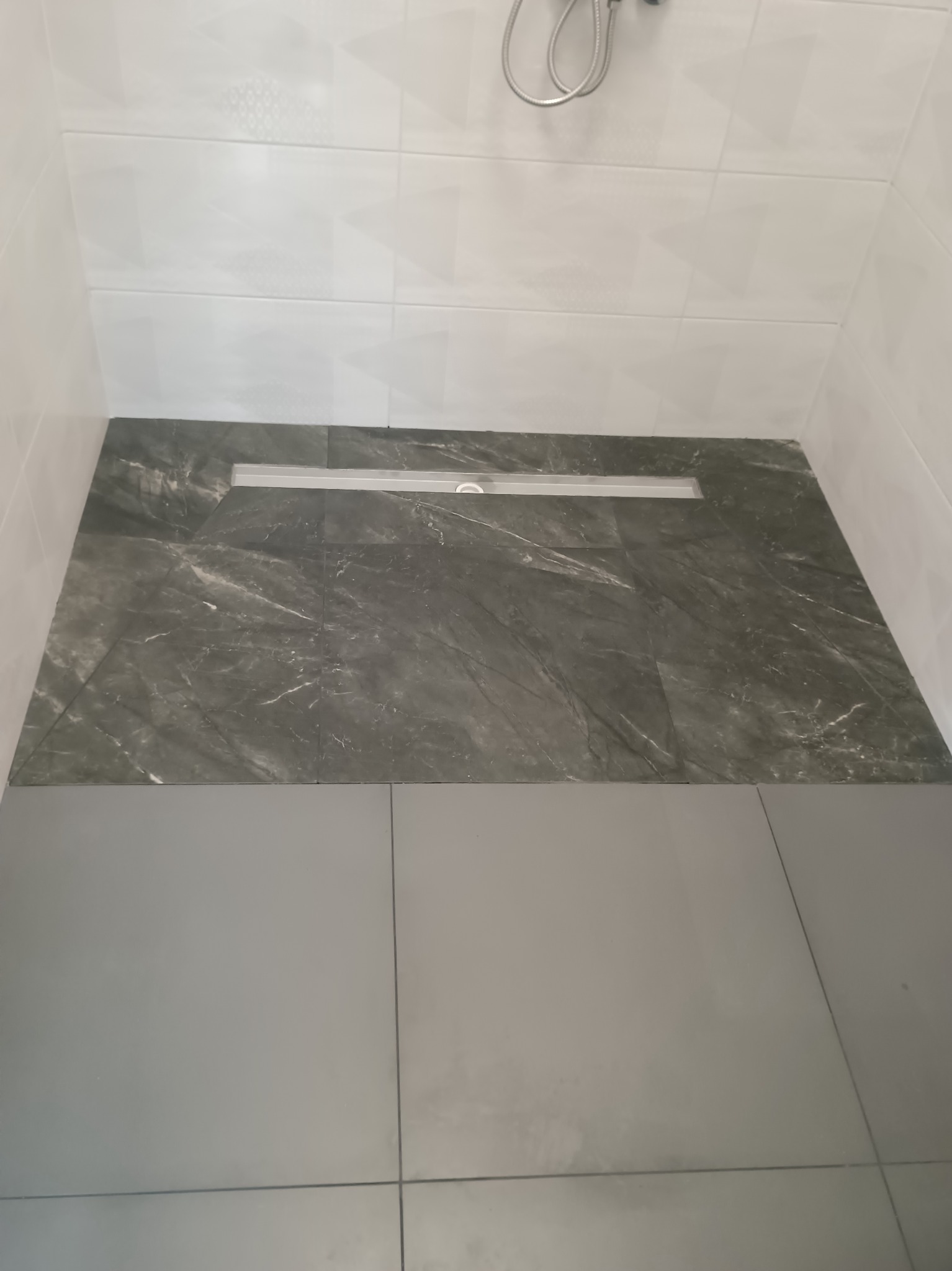 Wykończona strefa prysznicowa z odpływem liniowym i płytkami imitującymi marmur, w nowoczesnej łazience z białymi ścianami i deszczownicą.