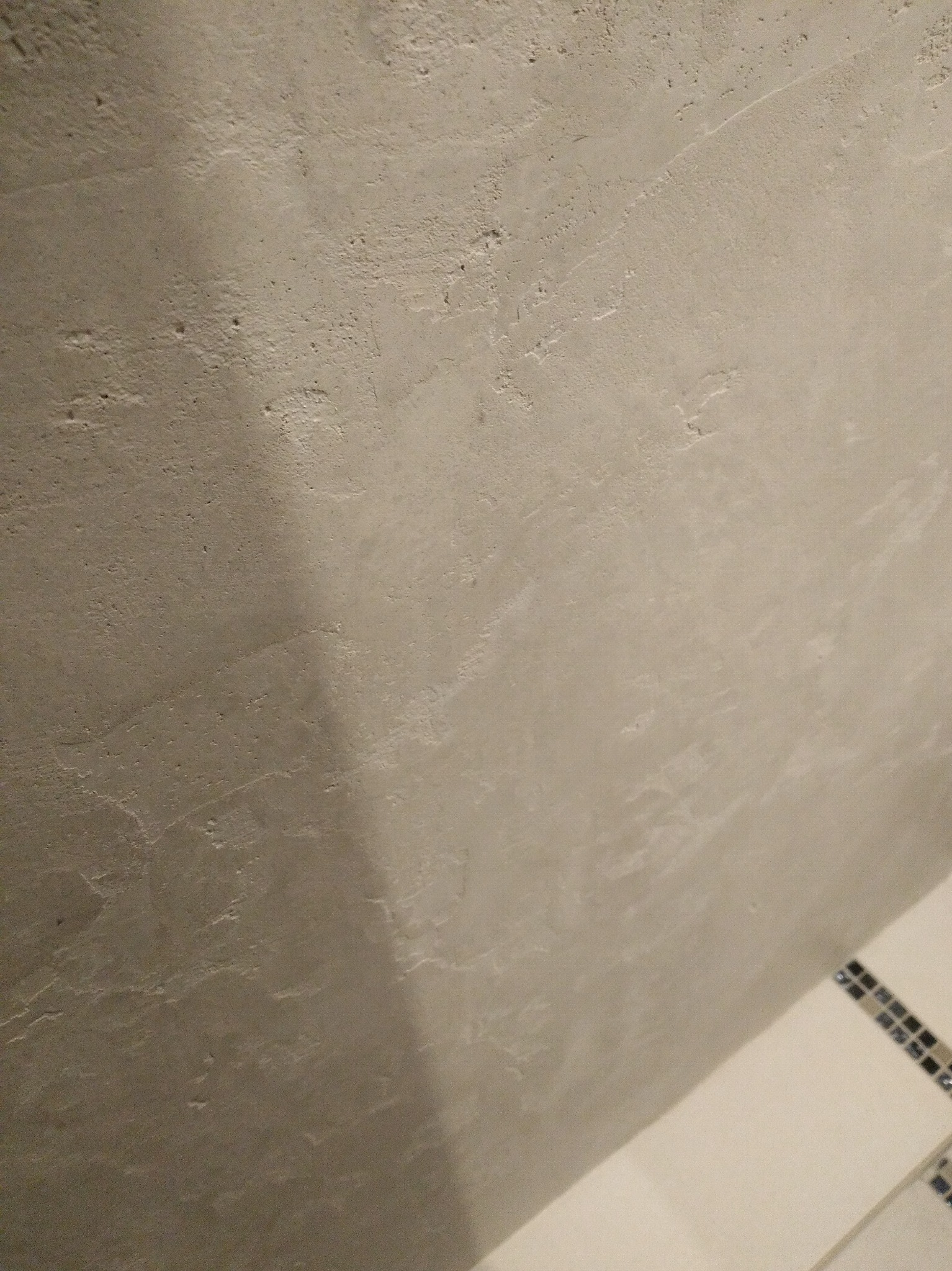 Szara ściana z efektem dekoracyjnym w łazience, widoczny fragment mozaiki. Bliski kadr, oświetlenie punktowe podkreśla fakturę ściany.