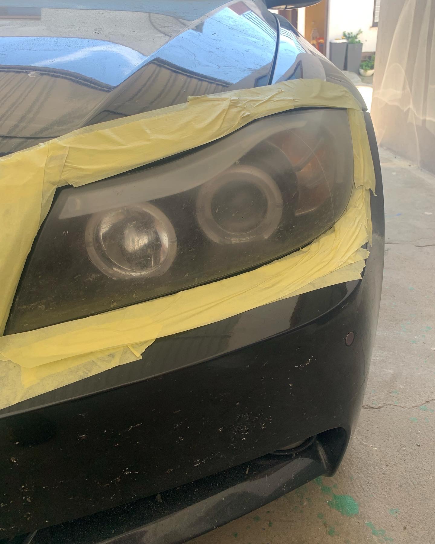 Przygotowanie reflektora samochodu do polerowania, zabezpieczonego żółtą taśmą maskującą, widoczne zmatowienie i drobne rysy na powierzchni klosza.