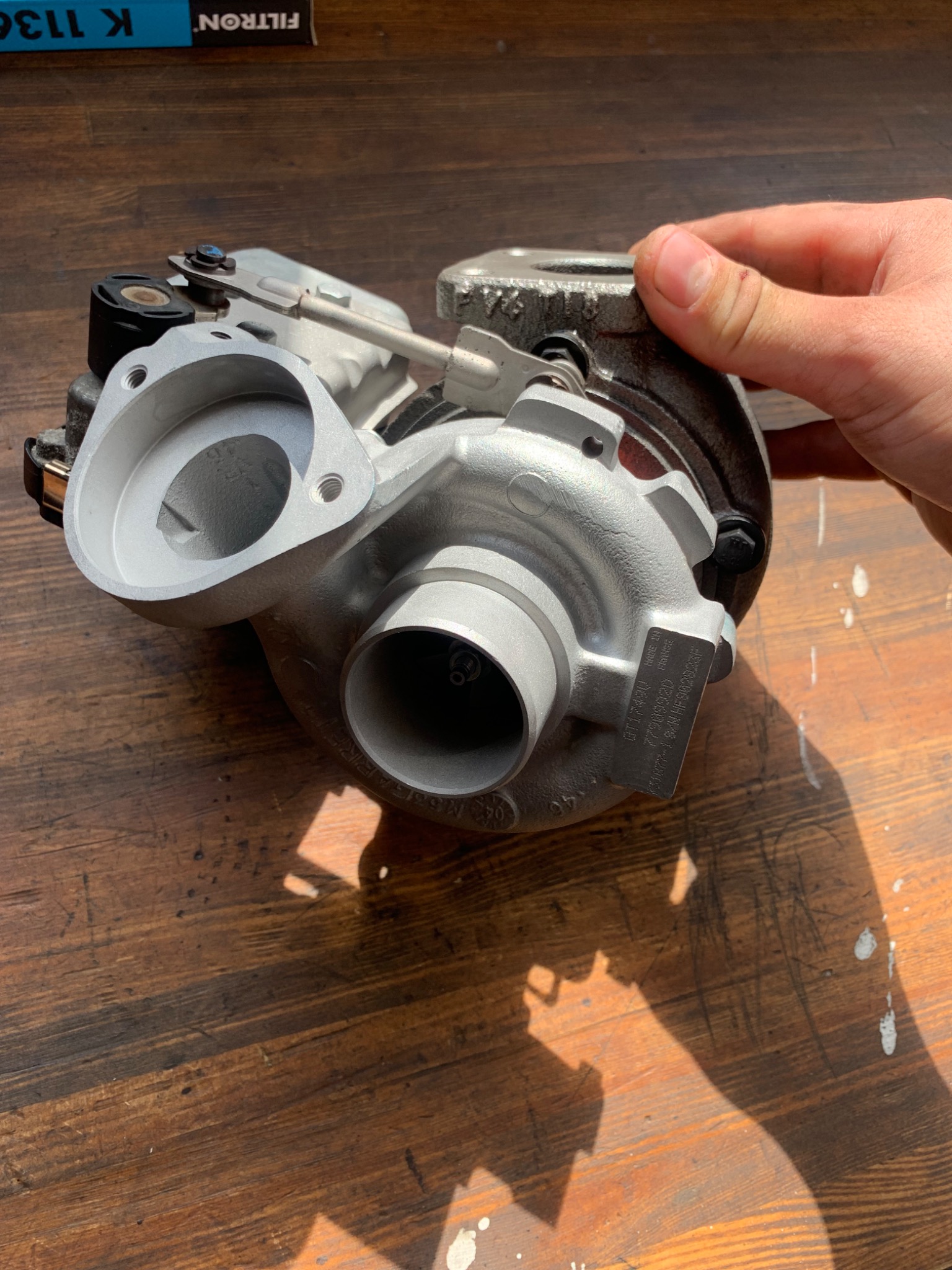 Nowa turbosprężarka samochodowa, trzymana w dłoni, widoczna na tle drewnianego stołu z wyraźnym cieniem, z widoczną tabliczką znamionową z napisem 'MADE IN FRANCE'.