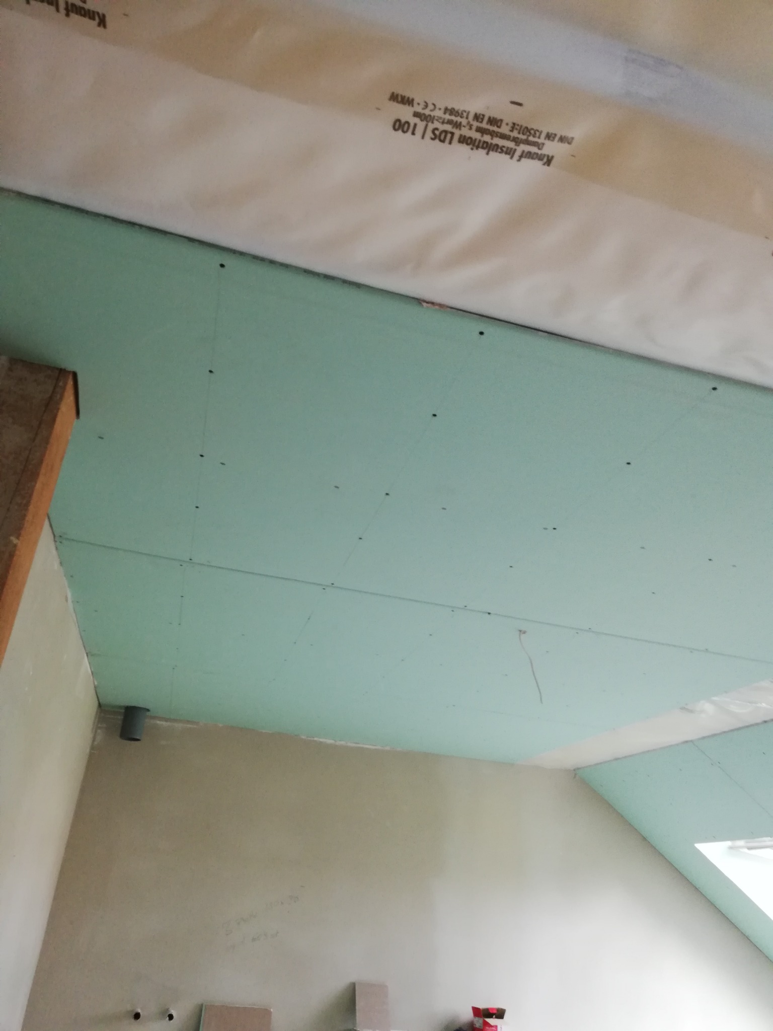 Montaż zielonych płyt gipsowo-kartonowych na suficie poddasza z widoczną izolacją Knauf, wstępny etap prac.