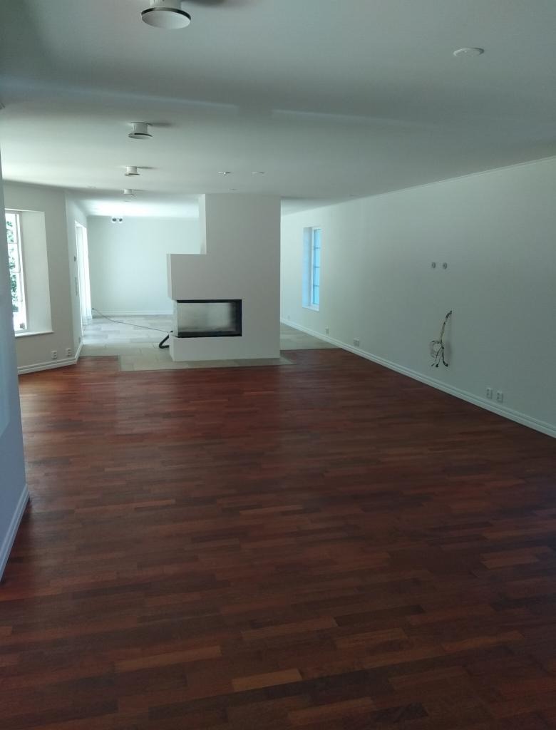 Salon po remoncie z nową, ciemną, drewnianą podłogą parkietową, białymi ścianami i nowoczesnym kominkiem z białej zabudowie.