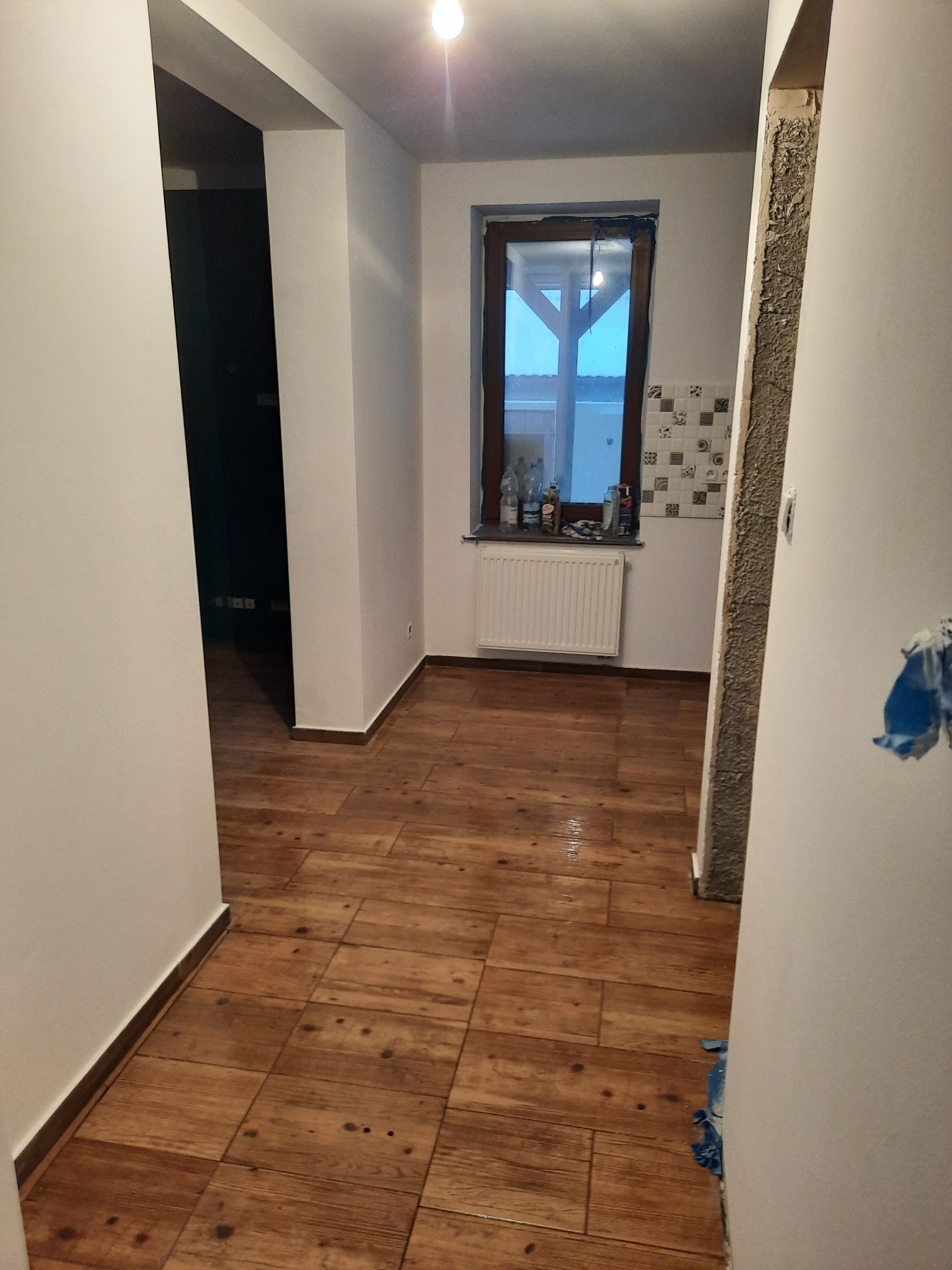 Układanie paneli podłogowych imitujących drewno w mieszkaniu w Poznaniu, widoczne przygotowane ściany do dalszych prac wykończeniowych, okno z grzejnikiem i butelkami na parapecie.