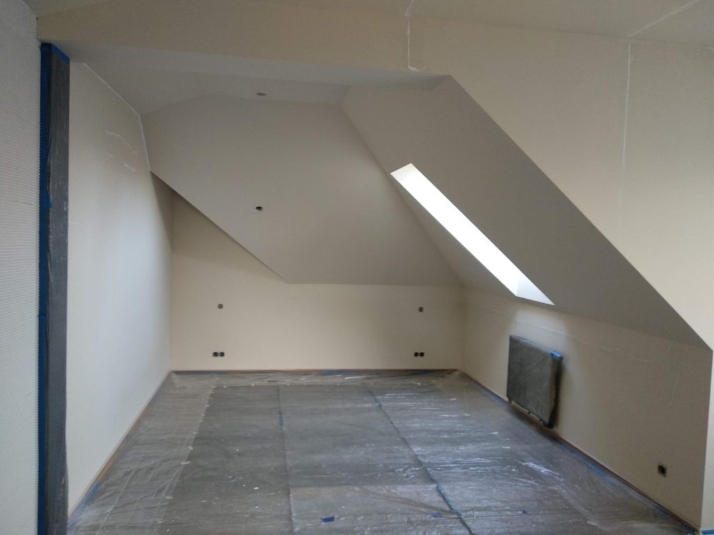 Poddasze po szpachlowaniu i malowaniu na biało, zabezpieczone folią malarską, z oknem dachowym i widocznymi punktami elektrycznymi.