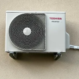 Zewnętrzna jednostka klimatyzacji Toshiba Inverter zamontowana na beżowej ścianie budynku, widoczne białe rurki instalacyjne.