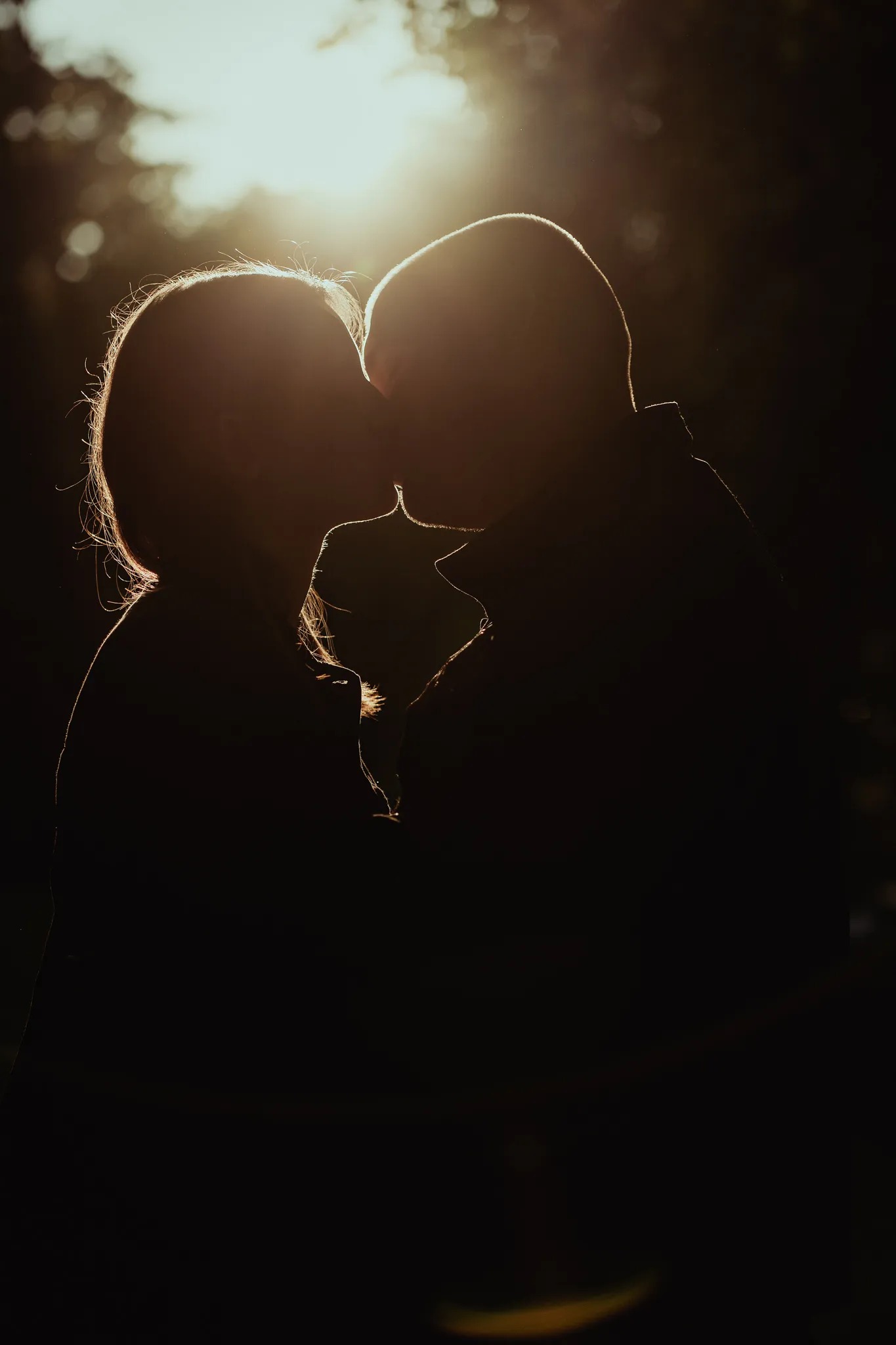 Silhouettes of a kissing couple backlit by the sun, creating a dramatic and romantic effect with a dark background.