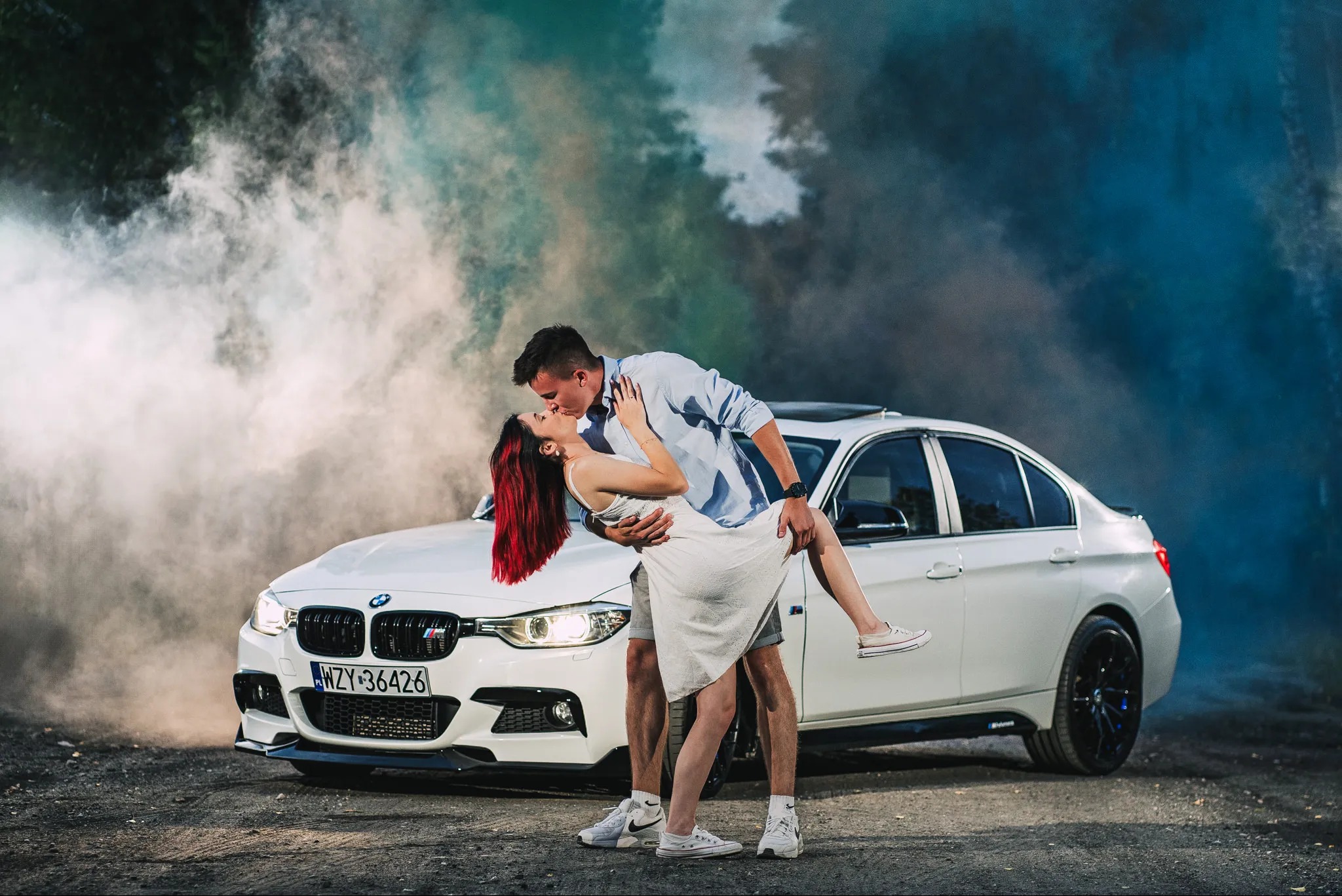 Zakochana para całująca się na tle białego BMW i kolorowych dymów
