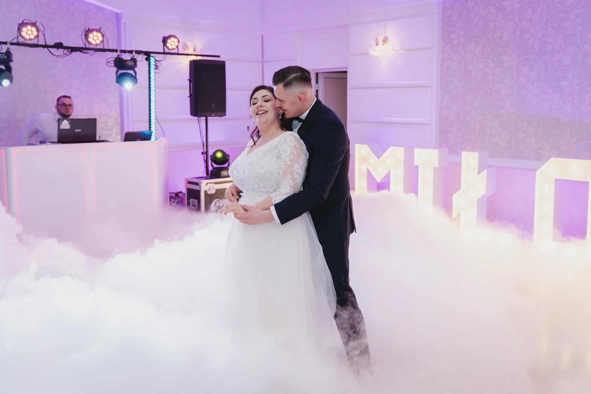 Para młoda w tańcu otoczona sztuczną mgłą, oświetlenie sceniczne w tle, dekoracyjne litery z żarówkami.