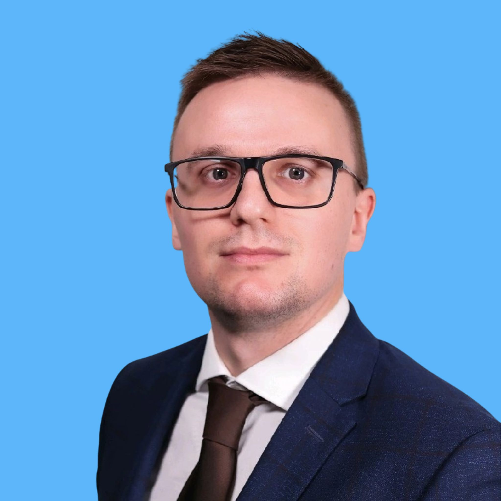 Portret mężczyzny w okularach i garniturze na jednolitym, błękitnym tle. Profesjonalny wizerunek.