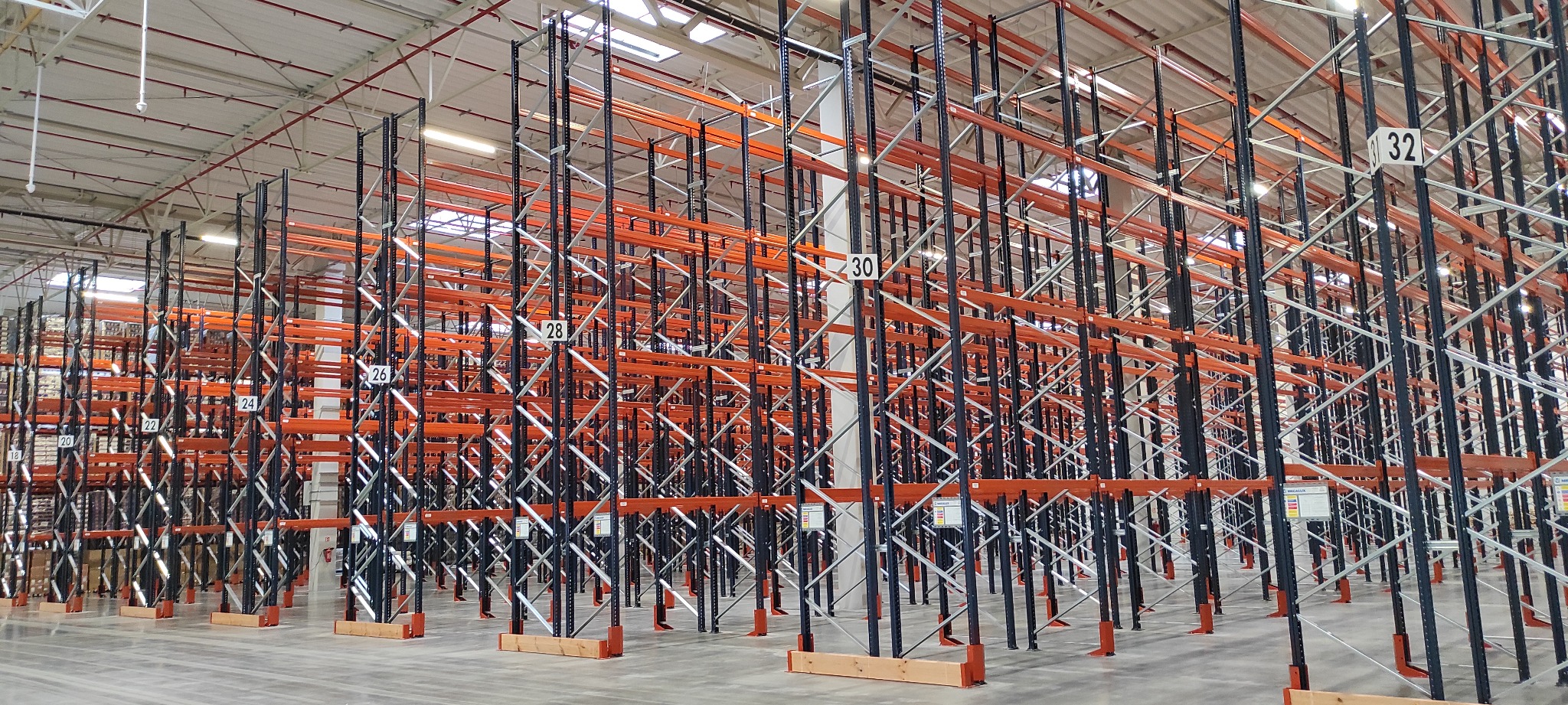 Puste, wysokie regały magazynowe z numeracją 24-32, widok z perspektywy podłogi, oświetlenie sufitowe