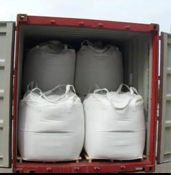 Wnętrze kontenera transportowego wypełnione czterema dużymi, białymi workami typu Big Bag, umieszczonymi na drewnianych paletach.