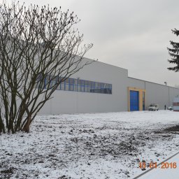 Zakład Ogólnobudowlany Bogdan Pociejewski - Nowoczesny budynek przemysłowy z szarej blachy trapezowej, niebieskie okna i brama, zimowy krajobraz z drzewami i śniegiem, ambulans na podjeździe.