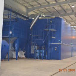 Zakład Ogólnobudowlany Bogdan Pociejewski - Duża, niebieska maszyna przemysłowa z systemem rur w hali fabrycznej, z widocznymi torami w podłodze i pracownikami w tle.