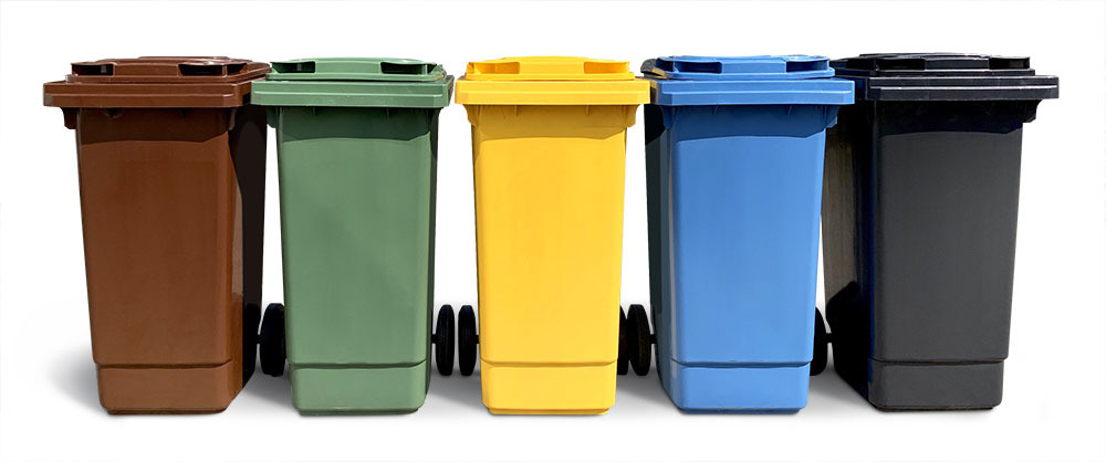 Rząd pięciu kolorowych kontenerów na śmieci z brązowym, zielonym, żółtym, niebieskim i czarnym wiekiem, ustawionych obok siebie na białym tle.