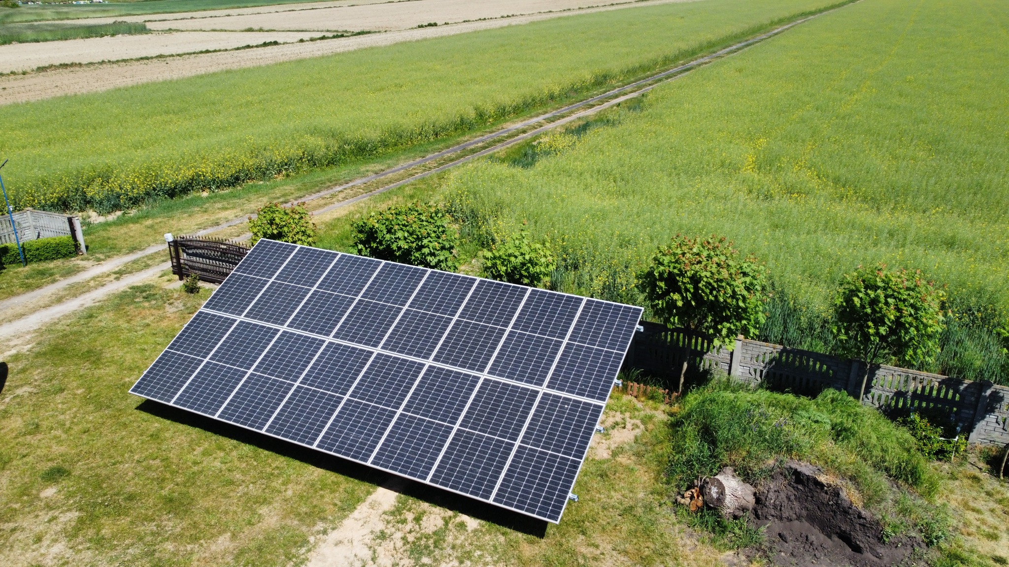 Panel słoneczny na trawniku, widok z góry, w tle pole uprawne i droga polna.