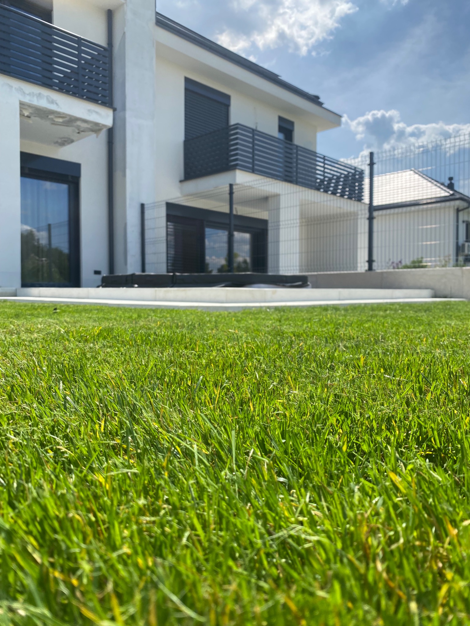 Wykonanie tarasu z bloków schodowych i płyt betonowych + realizacja ogrodu. Na zdjęciu widoczny taras i trawnik z rolki