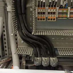 Szczegółowe ujęcie wnętrza szafy elektrycznej z widocznymi przewodami w peszlach, listwami zaciskowymi, oraz elementami montażowymi na szynach DIN.